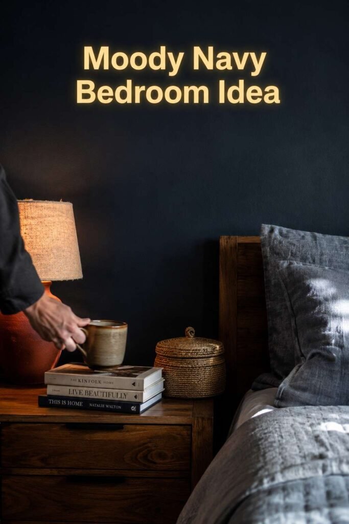 A man's hand sets a coffee mug on a nightstand styled with a rust lamp against a deep navy bedroom wall.