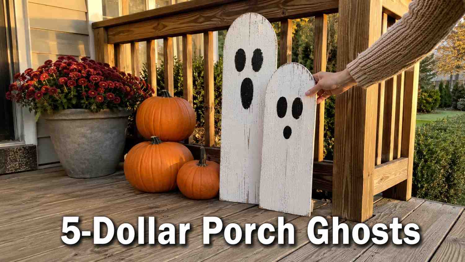 A pair of hand-painted wooden ghosts lean against a porch railing beside a small stack of pumpkins.