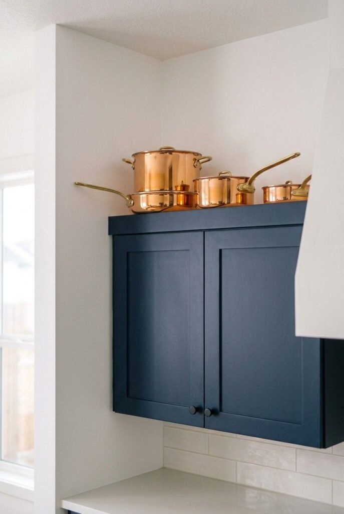 Polished copper pots displayed on top of navy blue kitchen cabinets.