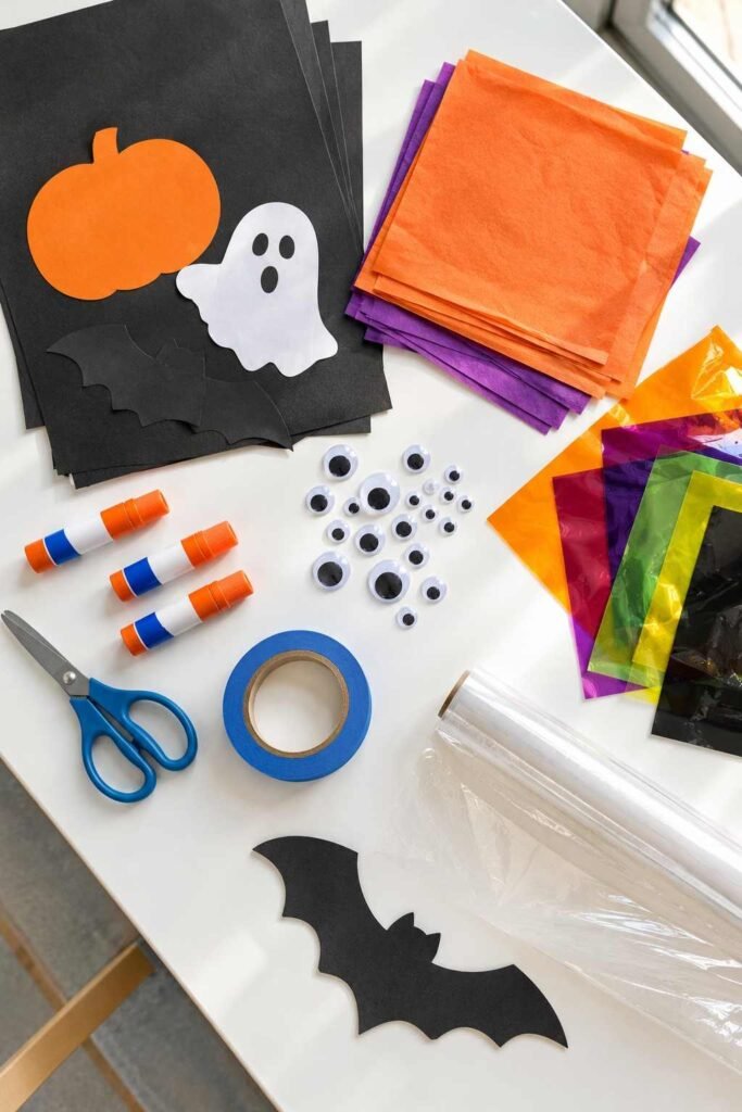 Flat lay of paper, tissue, cellophane, scissors, and tape used for school Halloween window decorations.