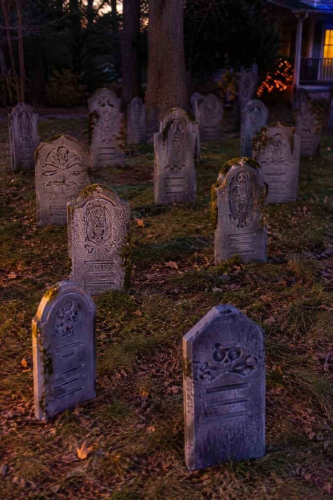 Rows of gray foam tombstones in a front yard at dusk with leaves and moss.