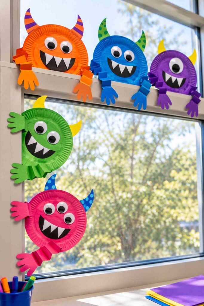 Painted paper plate monsters with googly eyes climbing over a school window frame.