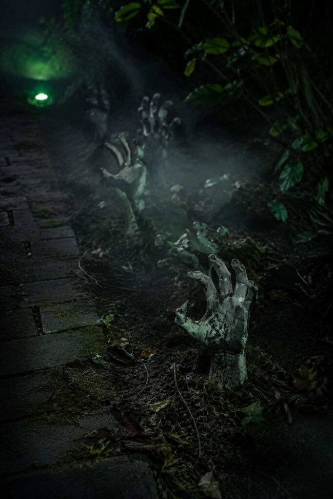 28 Halloween Party Decorations Scary Enough to Terrify Every Guest 8 Plaster zombie hands reaching from damp soil beside a path as outdoor Halloween party decor.